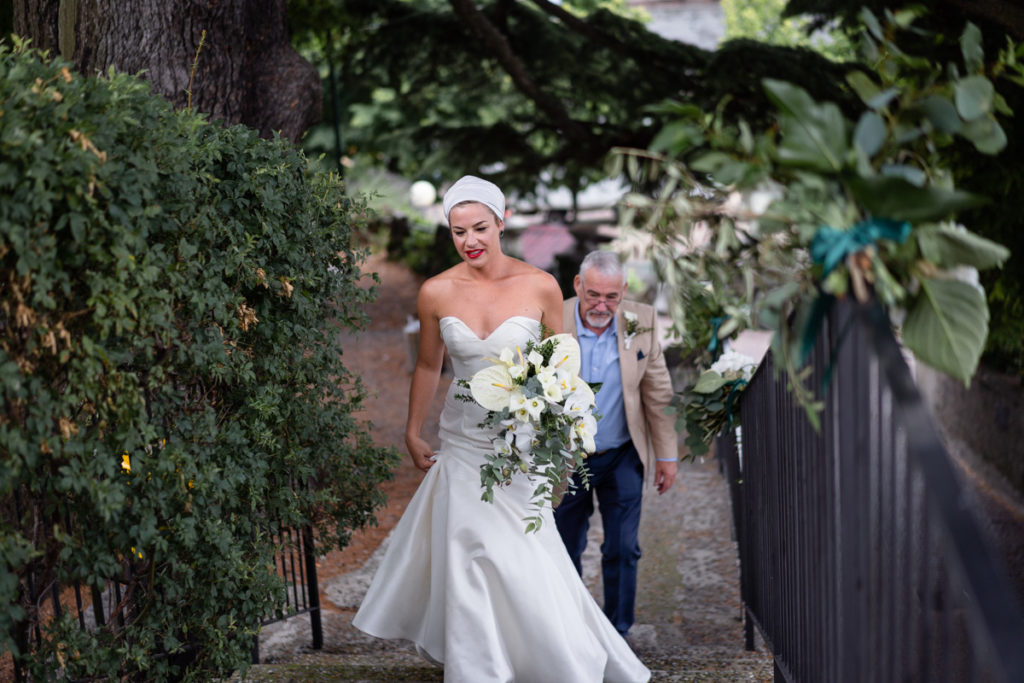 sposa che sale le scale con fiori in mano e dietro il padre